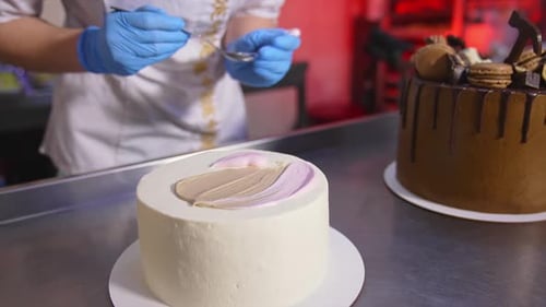Pastry cook applies white cream with a spoon on top of the white cake. Close up.