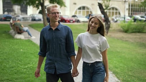 A Young Positive Couple Walks Holding Hands Meets in a Summer City Park