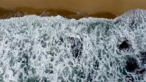 Turbulent sea waves meeting sandy shore, capturing the dynamic interface of water and land, aerial v