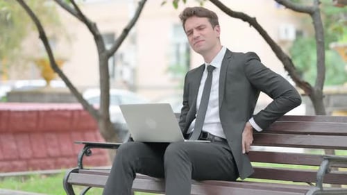 Man Works on Laptop With Back Pain Outside