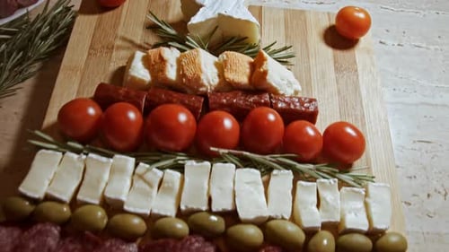 Planche à charcuterie avec salami tranché, saucisse fumée, fromage, tomates et olives disposées selon la forme