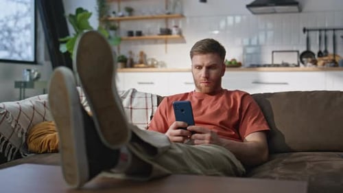 Man Relaxing on Couch Using Mobile Phone at Home