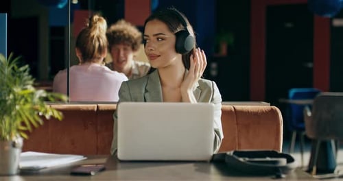 Adorable Young Woman in Wireless Earbuds Headphones Listens to Music Relaxes Sitting at Restaurant