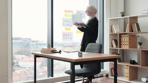 Female with Laptop Pointing at Charts on Office Window