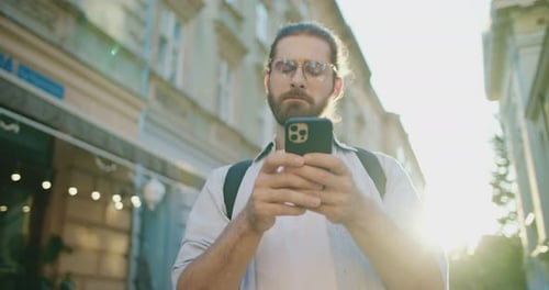 Side View of Handsome Young Adult Man Using Smartphone Working Online Standing on Urban Street