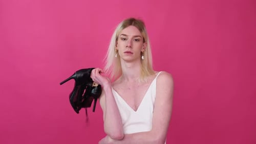 Transgender Man with Shoes Against Pink Background