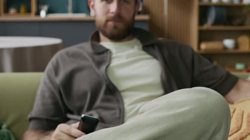 Man Sitting on Sofa Using Television Remote Control