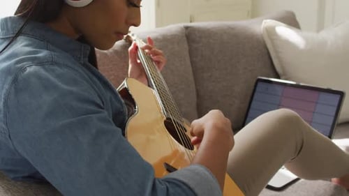 Woman Plays Guitar on Couch with Headphones