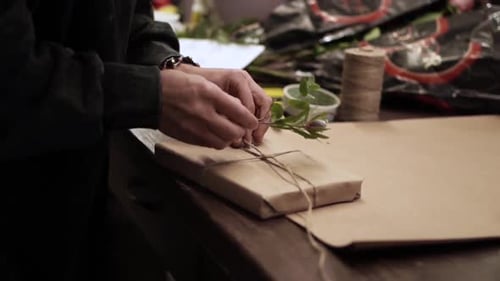 Hands Decorating Gift with Leaves and Twine