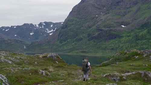 Backpacker Walking Towards The Lake By The Mountain In Norway During Winter, wide shot, static