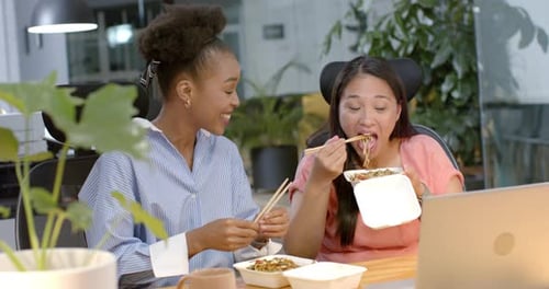 Young African American woman and biracial woman enjoy a business meal at the office