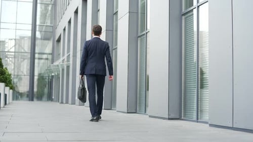 Businessman walking outside on the street near a city office building. Entrepreneur in a formal