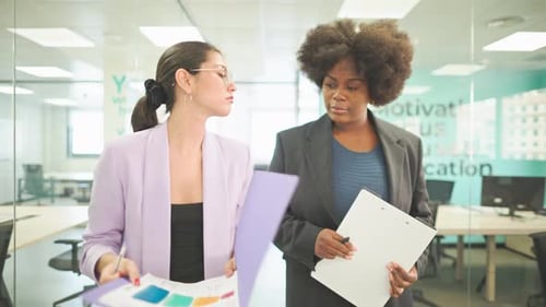 Two Businesswomen Discussing a Project While Walking in a Modern Office