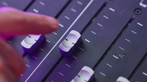 Close up on hand moving audio fader or slider on soundboard or mixer console in sound recording stud