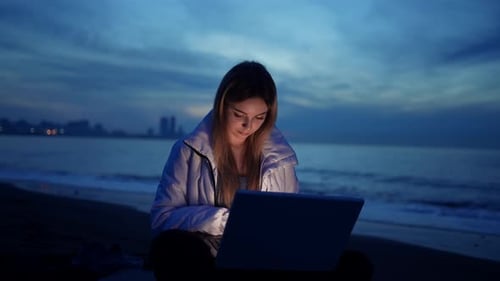 Retrato de una mujer independiente está usando una computadora portátil en la playa del mar por la noche