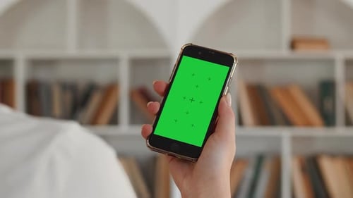Closeup of the Hand of a Young Woman Holding a Smartphone with a Mockup Green Screen Back View with