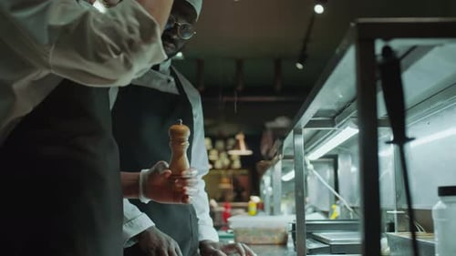 Professioneller Koch fügt gekochtem Steak in der Restaurantküche Salz und Pfeffer hinzu