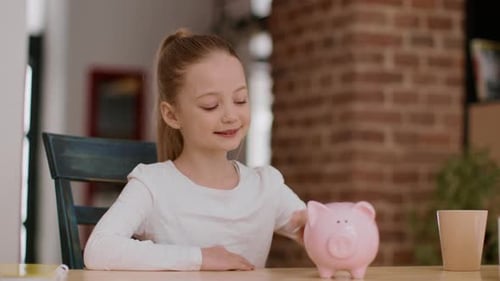 Entzückendes kleines Mädchen steckt Münze ins Sparschwein und klatscht zu Hause in die Hände und genießt ihren ersten