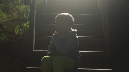 Boy Sits on Stairs in a Dimly Lit Area