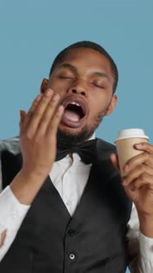 Vertical Video Hotel Concierge Staff Drinks Coffee While He is Yawning and Feeling Tired