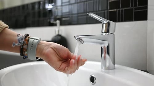 Woman Washing Hands at Sink in Bathroom