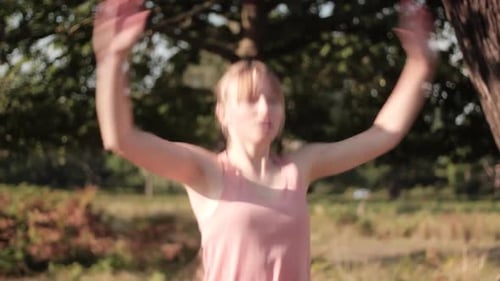 Woman doing Jumping Jacks up close in a park on a sunny day as the sun's rays fall on her face.