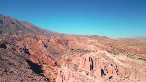 Aerial view drone flying over scenic red rocky mountains with a clear blue sky.