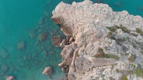 drone captures birds eye of rocky cliff edge, as camera soars over rugged landscape of blue water an