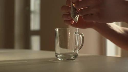 Close Up Side View of Unrecognizable Male Putting Bag of Drip Coffee in Glass Cup at Table in