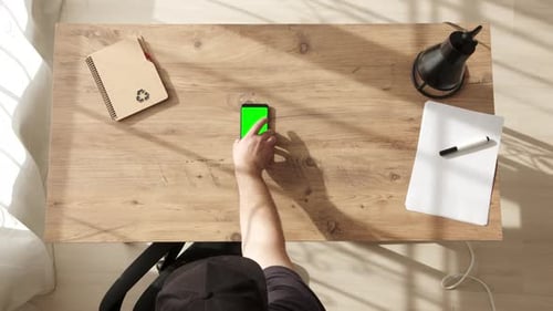 Man Put Mobile Phone with Green Screen on Desktop Top Down View