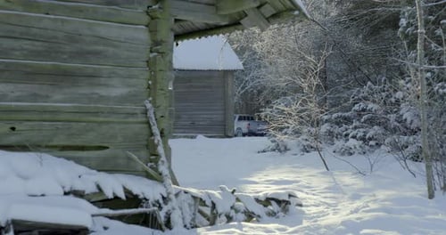 Wide shot of a log cabin covered in snow with a pickup truck in the background.
