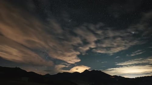Sterne und Wolken der Milchstraße bewegen sich im sommerlichen Sternenhimmel im Zeitraffer über die Alpen