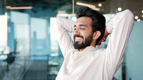 Close up. Young happy businessman relaxes with hands behind head while sitting at workplace
