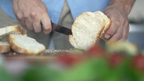 Mann schneidet in der Küche frisches Weißbrot mit einem scharfen Messer in Scheiben, um ein leckeres Essen zuzubereiten