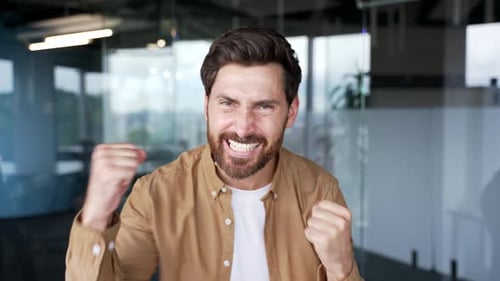 Excited happy handsome businessman celebrating success looking at camera in a modern business office