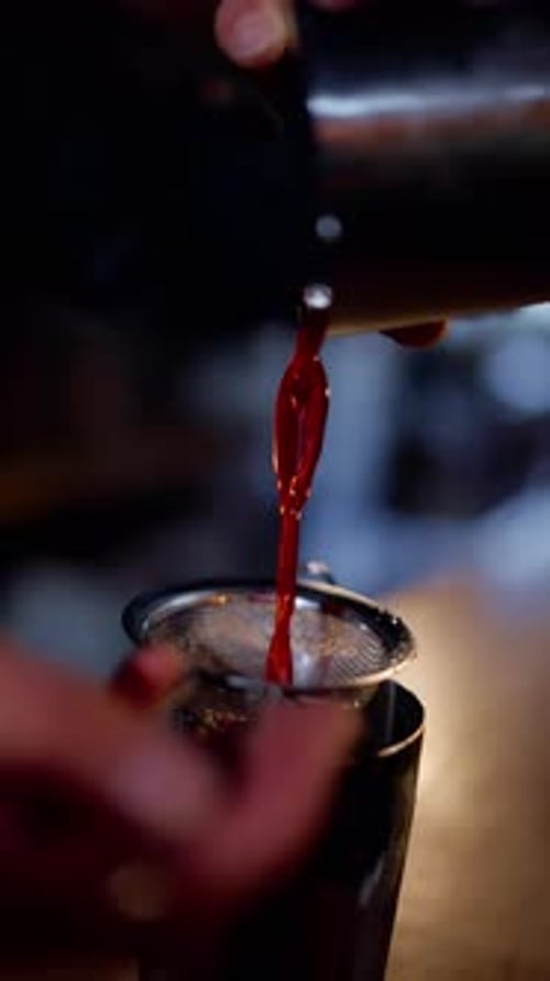 Bartender Pouring Red Cocktail Through Strainer at Bar