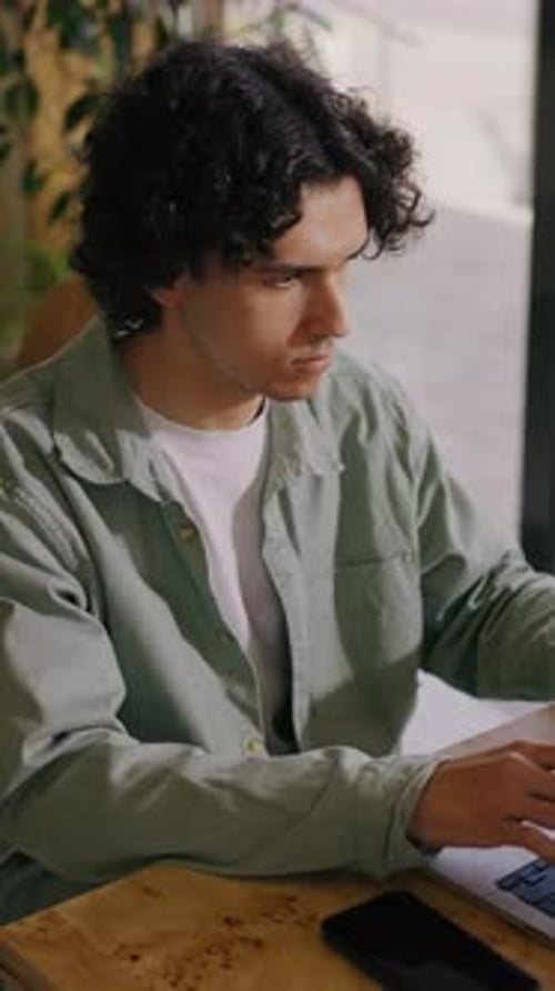 Focused Young Man Working at Laptop in Cozy Indoor Workspace with Natural Light Concentrating on