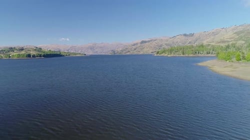Dynamischer Drohnenflug von hinten nach vorne über einen Stausee, immersive Luftaufnahme