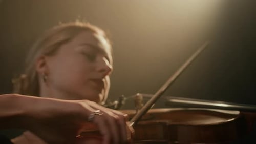 Blonde Woman Playing Violin in Dark Setting