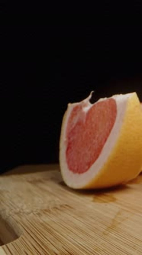 Vertical video. Slices of grapefruit on a black background. I take a bite of one slice.