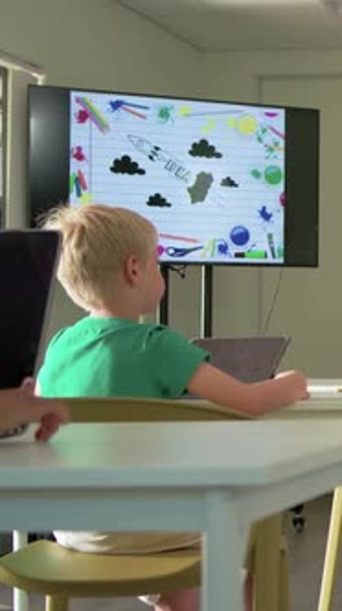 Vertical video: Seeing rocket on screen, boy green shirt shifting tablet and raising hand at school