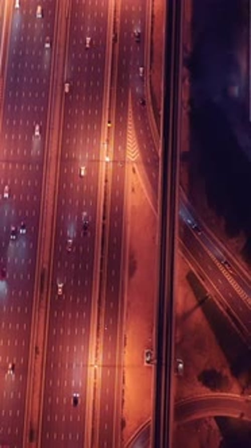 Vue de dessus de la circulation nocturne rougeoyante qui traverse les échangeurs autoroutiers entourés de paysages futuristes