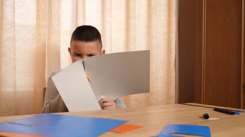 Boy Carefully Cutting Paper with Scissors at Table