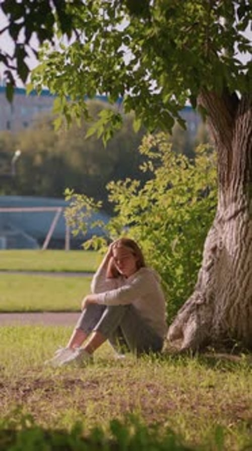 Thoughtful Woman Sitting Under Tree with Stadium Background