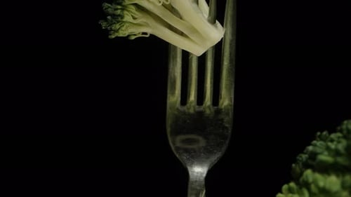 Broccoli on a fork rotates on a black background. Dolly slider extreme close-up.