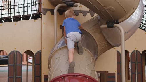 A Little Boy Rides Down a Slide on a Playground Near the House