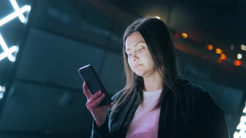 Woman Using Smartphone at Night Under Neon Lights
