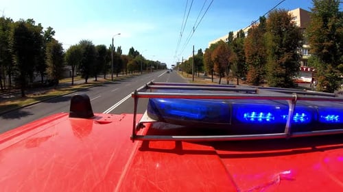 Big Red Truck with Blue Flashing Warning Light Riding to Place of a Fire on Urban Road Fire Engine