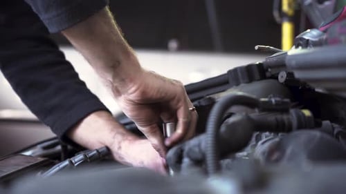 jeune mécanicien automobile répare un moteur de voiture. Remplacement de bougies d'allumage.