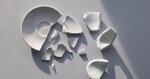 Pieces of broken saucer and cup on light grey background, flat lay. Camera moving forward